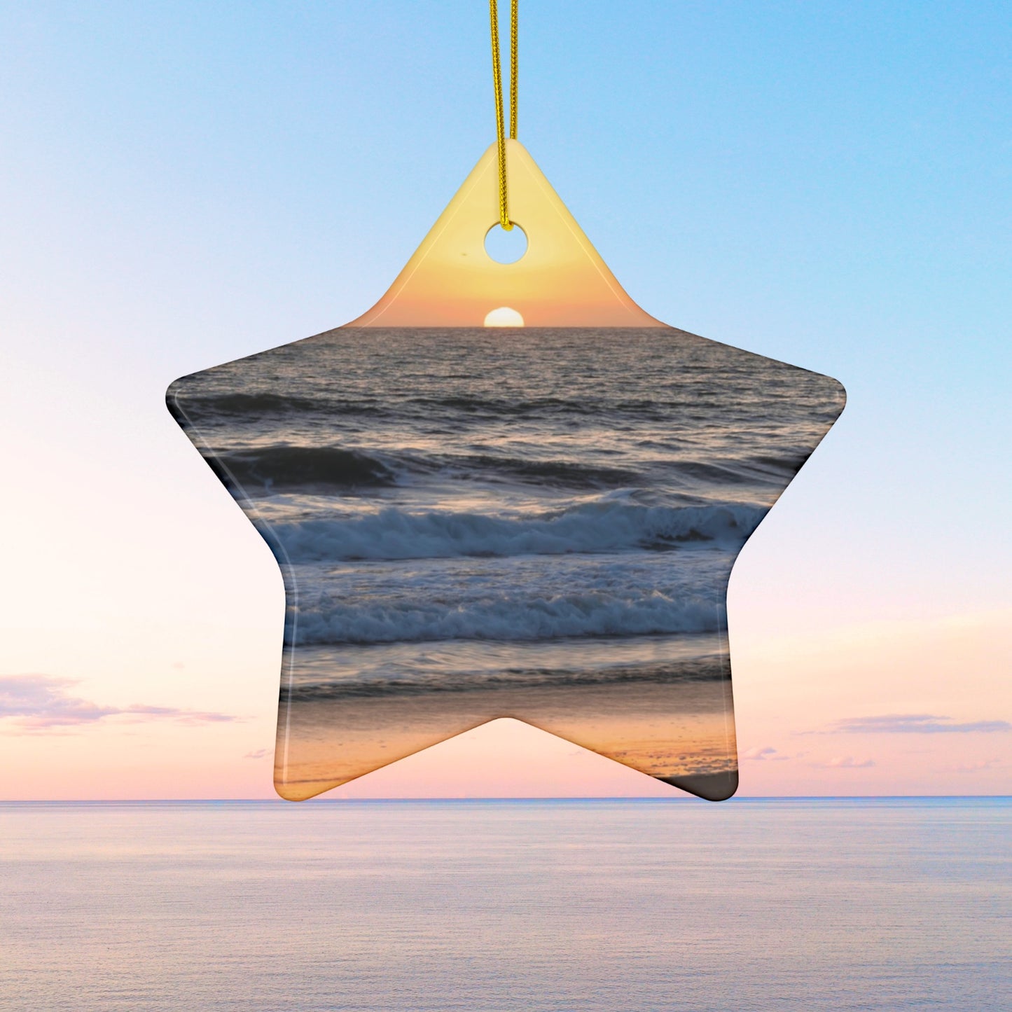 Star-shaped ceramic Christmas ornament featuring a photograph of a vibrant amber and gold sunset over the Pacific Ocean with waves rolling toward the shore.