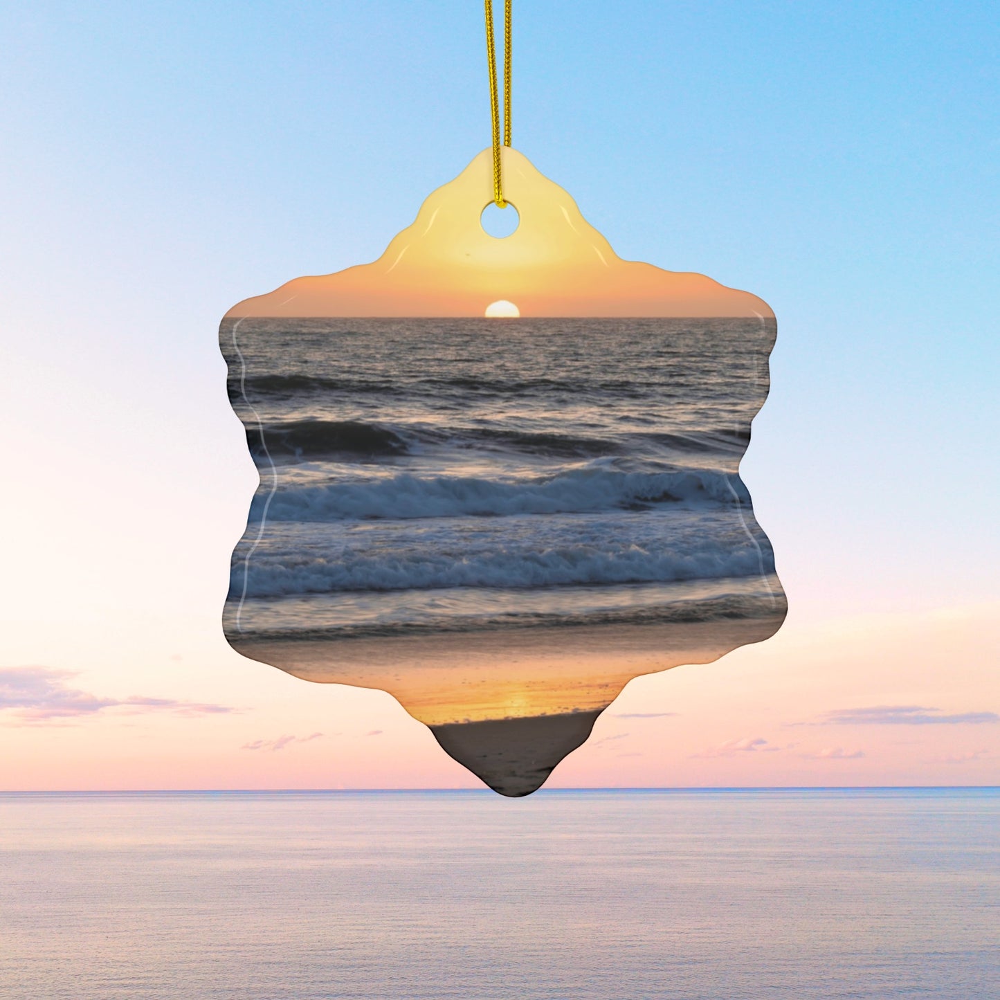 Ceramic Christmas ornament featuring a photograph of a vibrant amber and gold sunset over the Pacific Ocean with waves rolling toward the shore.