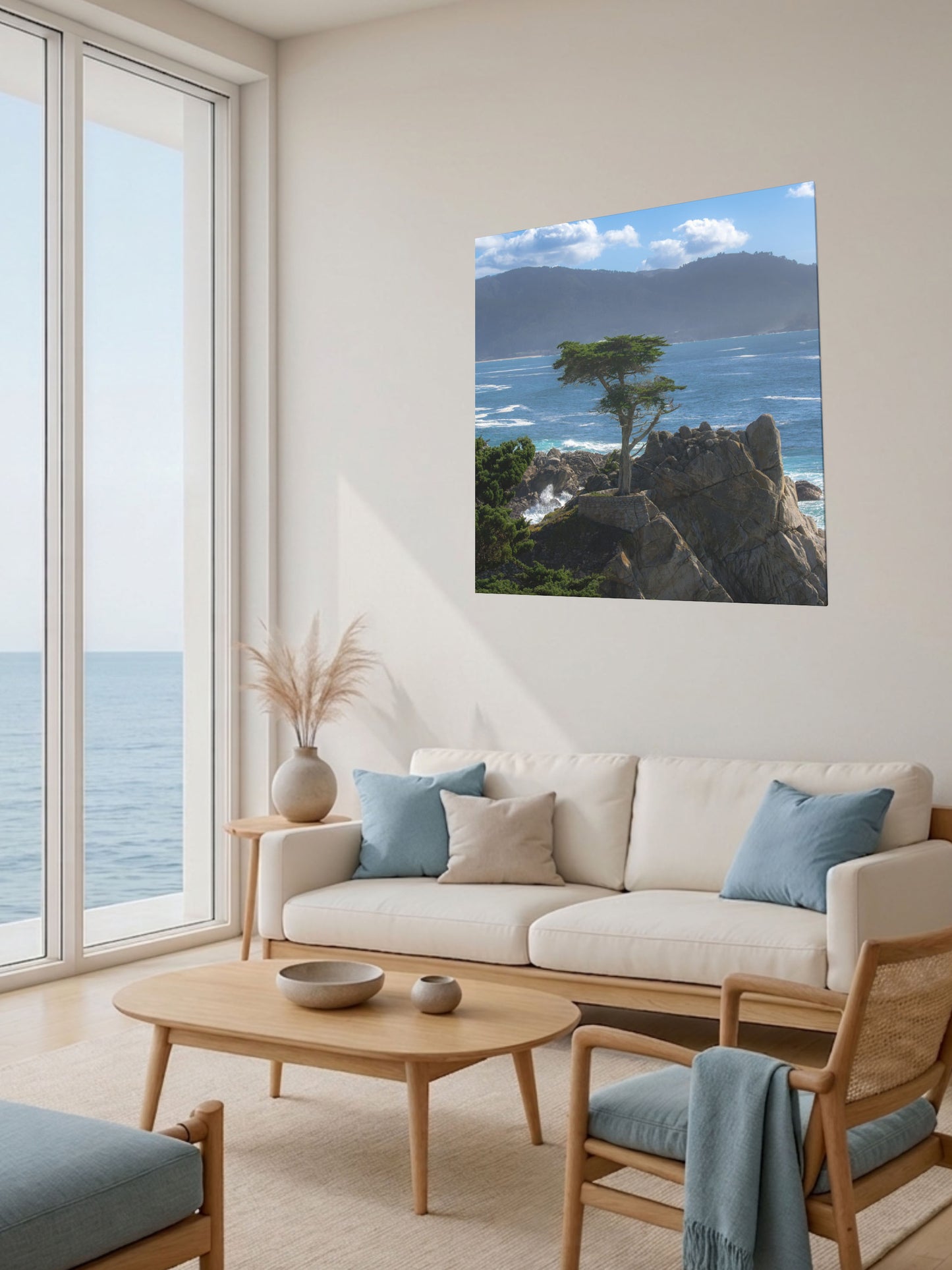 Living room with a large window view of the ocean, a beige sofa with blue cushions, and a canvas print of the lone cypress tree at Pebble Beach on a rocky cliff.