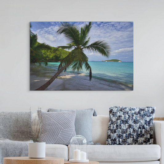 A canvas print of a tropical beach sceneon a wall above a sofa with decorative pillows.