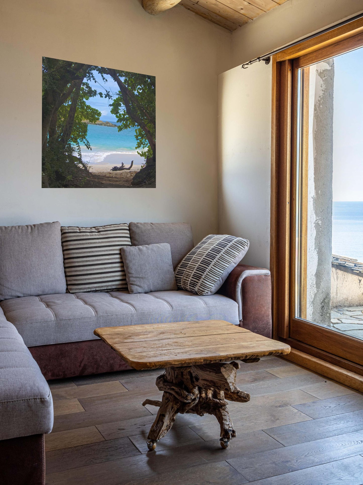 Living room with a gray sofa, wooden coffee table, and a tropical beach view through trees Hawaiian island canvas print