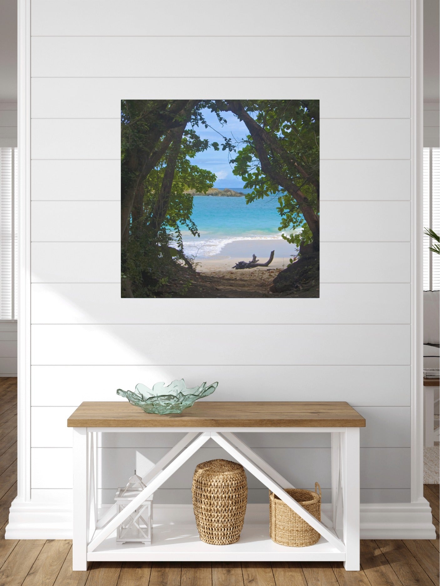 Tropical beach view through trees Hawaiian island canvas print on a white wall above a wooden bench.