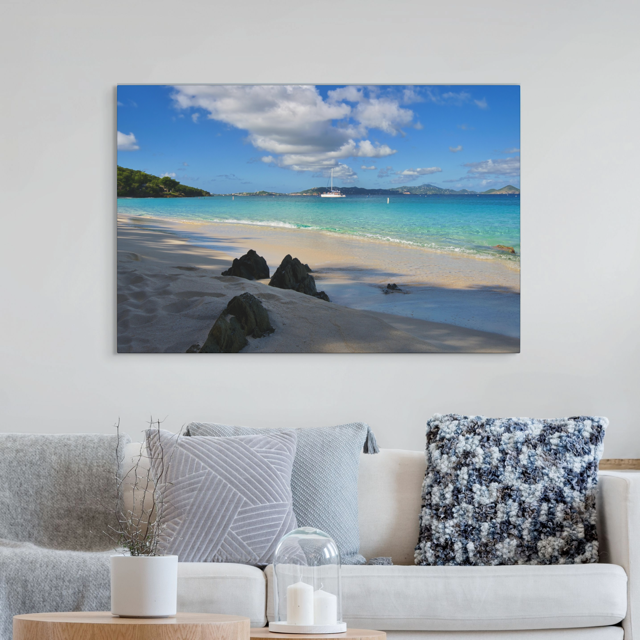 A canvas print of a tropical beach scene on a wall above a sofa with decorative pillows.