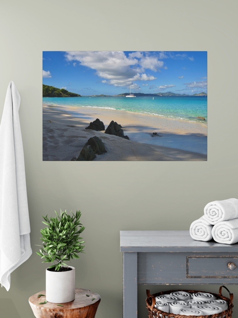 A canvas print of a tropical beach scene on a wall above a table with towels and a plant.