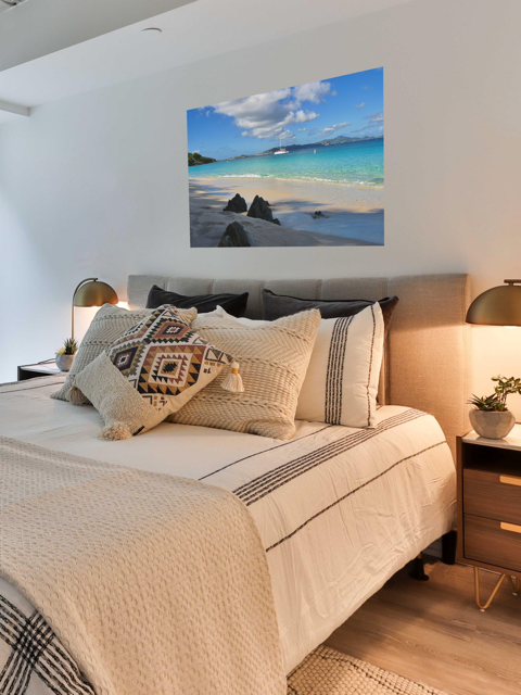 Bedroom with a bed featuring patterned pillows and a large wall art of a tropical beach scene.