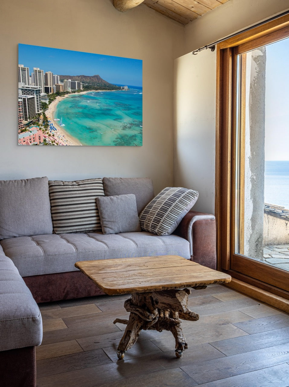 Living room with a large window and a canvas print of an overhead view of the beach and hotels on Waikiki Beach in Hawaii with Diamond Head in the background on the wall.