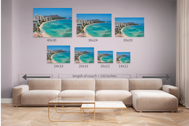 Wall art prints of an overhead view of the beach and hotels on Waikiki Beach in Hawaii with Diamond Head in the background with corresponding dimensions displayed above a beige sofa.