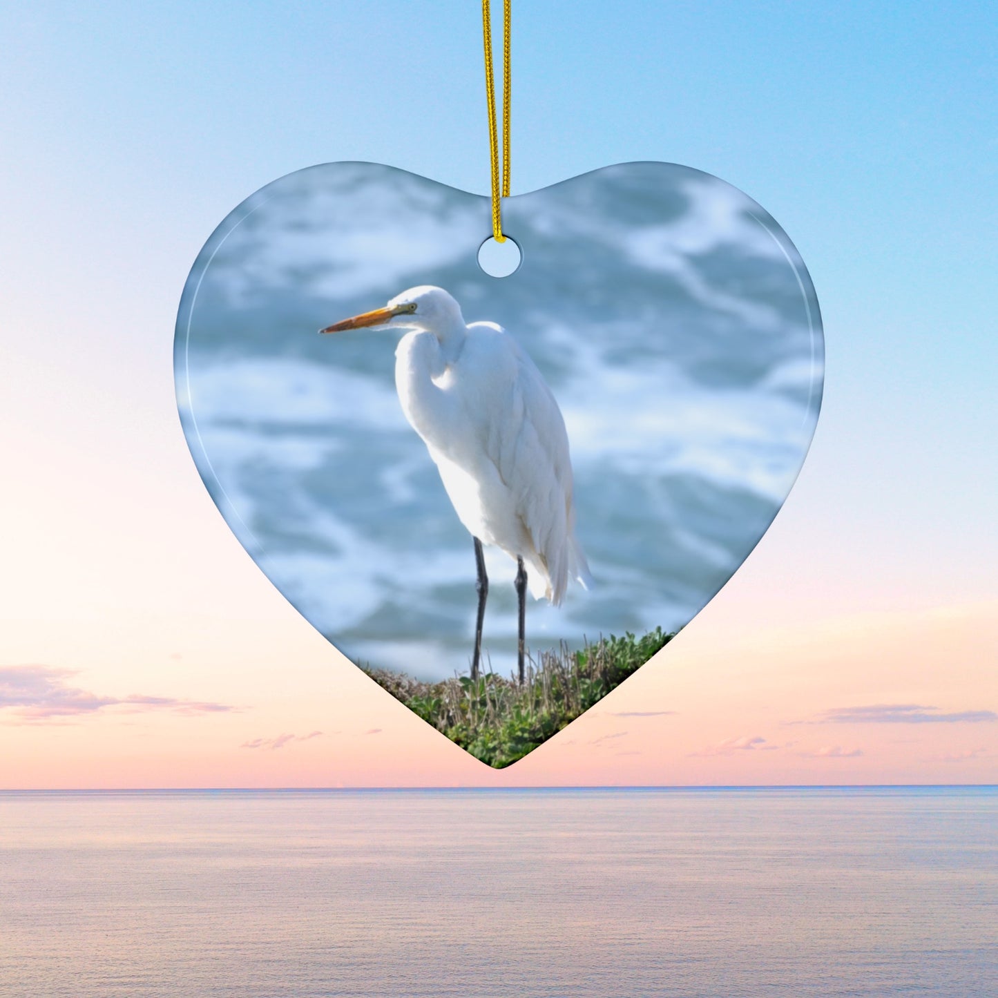 Heart-shaped ceramic holiday ornament featuring a  photograph of a White Egret on a cliff overlooking blue ocean waves with sea spray