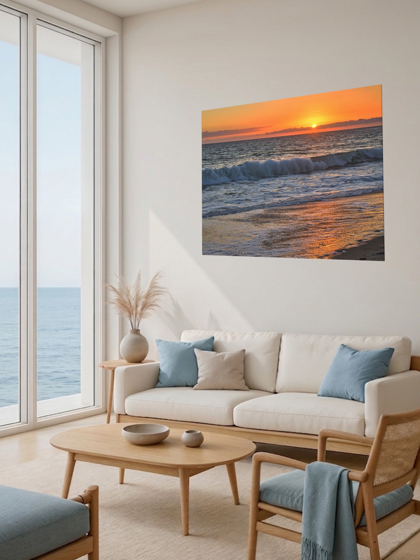 Modern living room with a large window view of the ocean, featuring a beige sofa with blue cushions and a canvas print of a Zuma Beach sunset in Malibu California with golden sky and reflective sand.