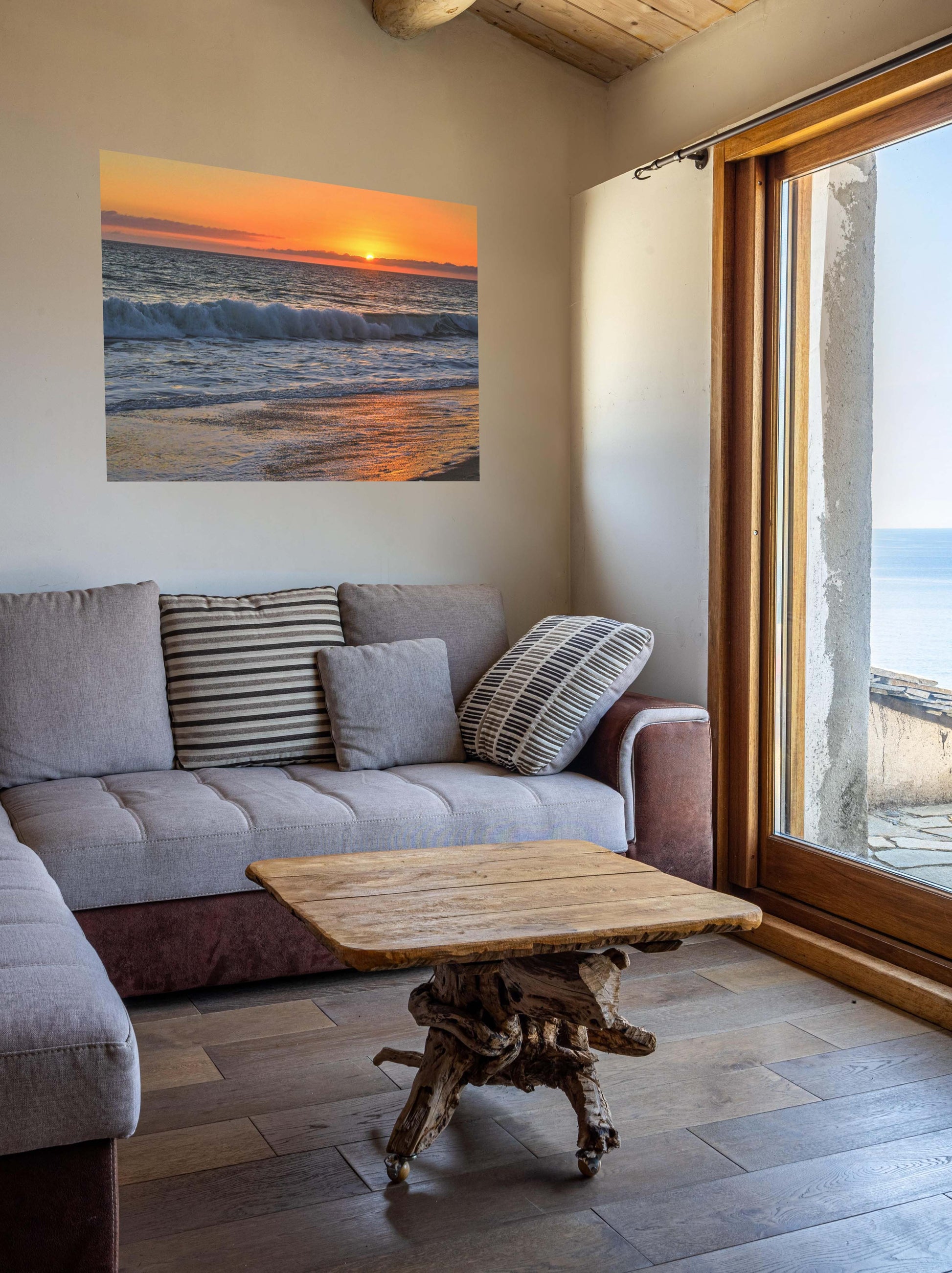 Living room with a gray sofa, wooden coffee table, and a canvas print of a Zuma Beach sunset in Malibu California with golden sky and reflective sand.