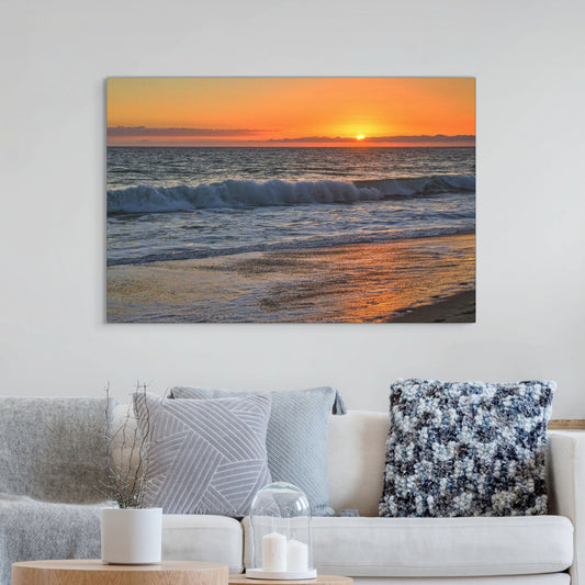 Canvas print of a Zuma Beach sunset in Malibu California with golden sky and reflective sand hanging on a wall above a sofa.